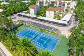 Vista aérea de una zona residencial con cancha de tenis, rodeada de abundante vegetación y edificios modernos.
