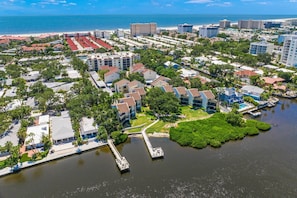 Vista aérea de una zona residencial costera con un puerto deportivo, que muestra una combinación de casas unifamiliares y edificios de apartamentos, un muelle y una playa al fondo.