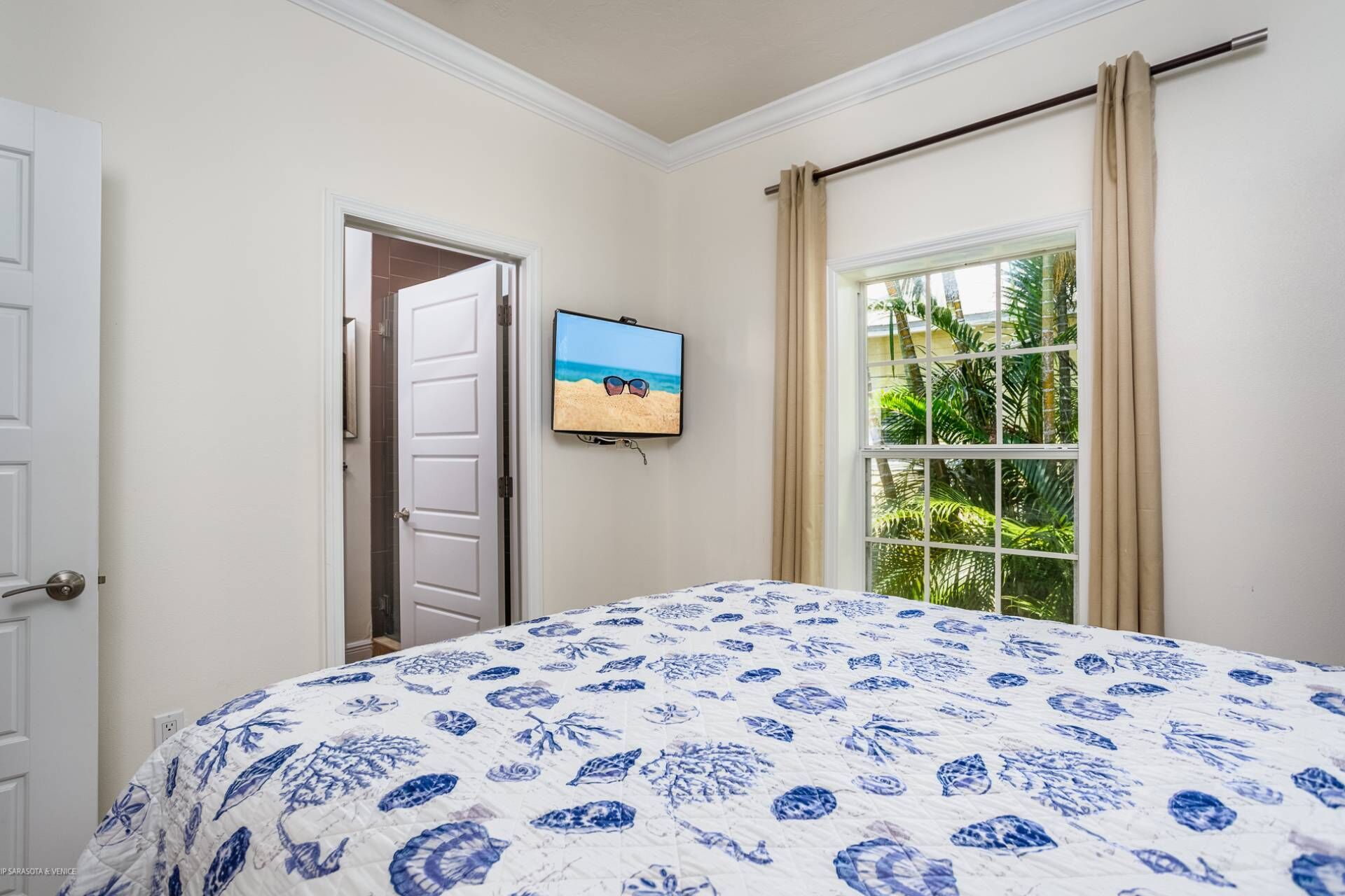 Een slaapkamer met een bed, een televisie aan de muur, een deur en een raam met gordijnen.