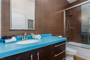 Een badkamer met een blauw aanrecht, een witte wastafel, een spiegel, een douche en een toilet.