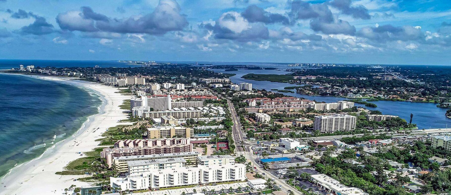 An aerial view of a coastal city with a beachfront, dense urban area, and a river.