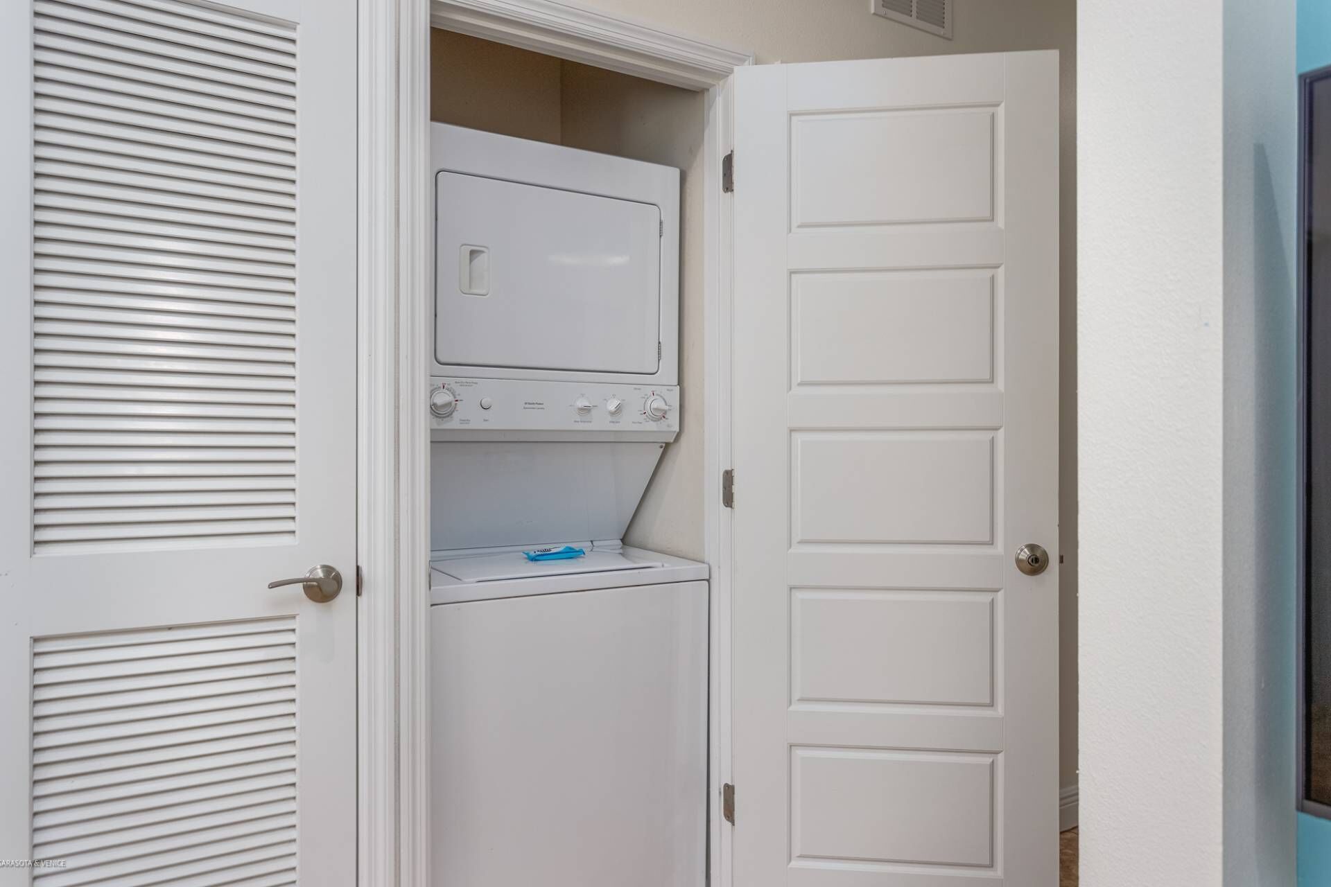 A laundry room with a front-loading washer and dryer, a door with a handle, and a vent above the dryer.