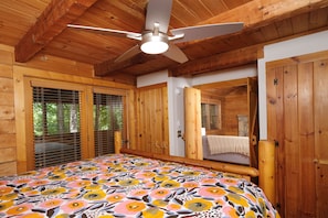 Un dormitorio de cabaña de madera con cama, ventilador de techo y puertas de madera.