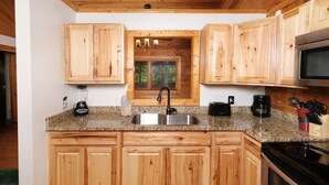 Una cucina con mobili in legno, piani in granito, lavello in acciaio inox, piano cottura nero e forno a microonde.