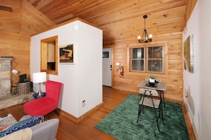 Interior acogedor de una cabaña con una silla roja, una mesita con una lámpara y una alfombra verde.