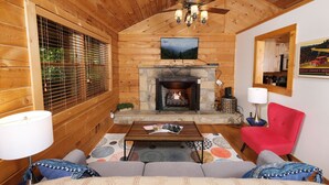 Un accogliente interno di una baita in legno, con un caminetto e una televisione sopra, e una poltrona rossa.