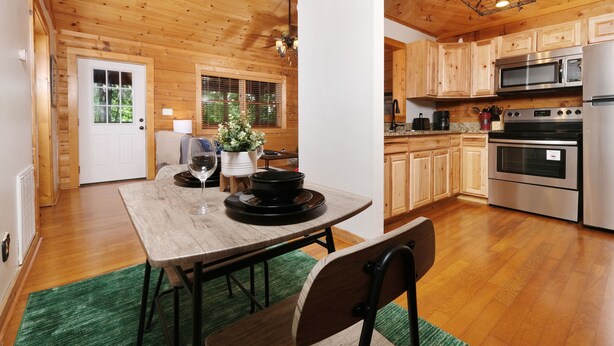 Un interno in legno con un tavolo da pranzo, sedie, una cucina con pensili in legno, un forno a microonde e un forno.