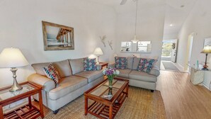 A living room with a sofa, two side tables, a coffee table, a ceiling fan, a painting, and a view of the kitchen. - Hickory on the Golf Course (Sarasota)