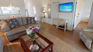 A living room with a sofa, a coffee table with flowers, a TV, and a door leading to another room. - Hickory on the Golf Course (Sarasota)