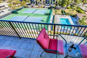 Un balcon donnant sur un court de tennis, une piscine et un espace salon extérieur.