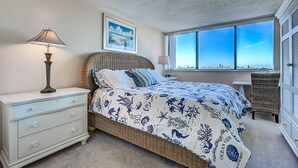 A bedroom with a bed, nightstands, a lamp, a framed picture, a window with a view, and a dresser.