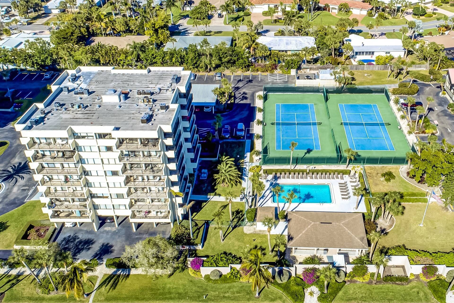An aerial view of a hotel with multiple floors, outdoor seating areas, a tennis court, and a swimming pool.