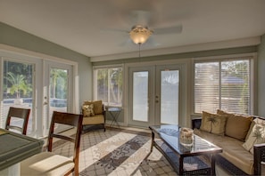 A sunlit room with a ceiling fan, a dining table with chairs, a sofa, and a coffee table.