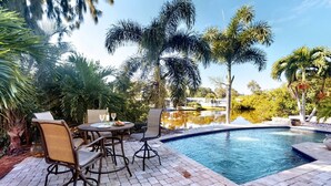 A pool area with a table and chairs, surrounded by palm trees and a clear sky. - Peacock Bungalow - Left (Siesta Key)