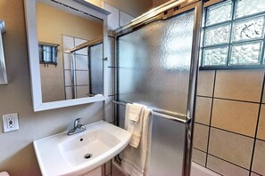 A bathroom with a white sink, a mirror, a towel hanging on a rack, and a frosted glass shower enclosure.
