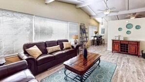 A living room with a leather sofa, wooden coffee table, and a dining area with a red cabinet. - Peacock Bungalow - Left (Siesta Key)