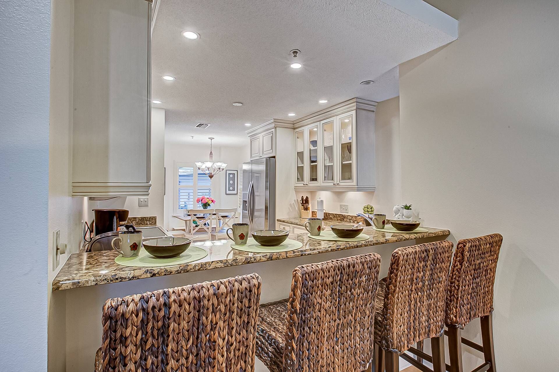A kitchen with a long island, white cabinets, and a stainless steel refrigerator.