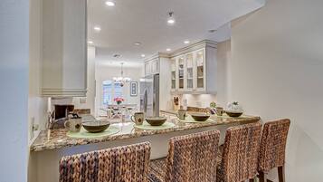 A kitchen with a long island, white cabinets, and a stainless steel refrigerator.