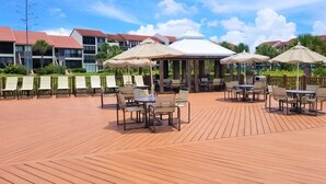 A wooden deck with outdoor seating and umbrellas, surrounded by buildings with red roofs. - Siesta Dunes on Siesta Key (Siesta Key)