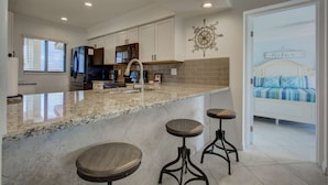 A modern kitchen with a granite countertop, stainless steel appliances, and a breakfast bar with stools. - Siesta Dunes on Siesta Key (Siesta Key)