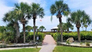 A pathway leading to a covered area with palm trees and a view of the ocean. - Siesta Dunes on Siesta Key (Siesta Key)