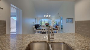 A kitchen with granite countertops, stainless steel sink, and a dining area with a table and chairs. - Siesta Dunes on Siesta Key (Siesta Key)