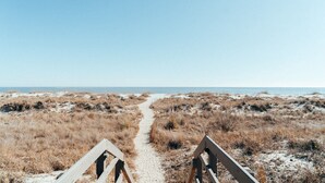 Ein Strandweg führt zum Meer, gesäumt von Sand und trockenem Gras.