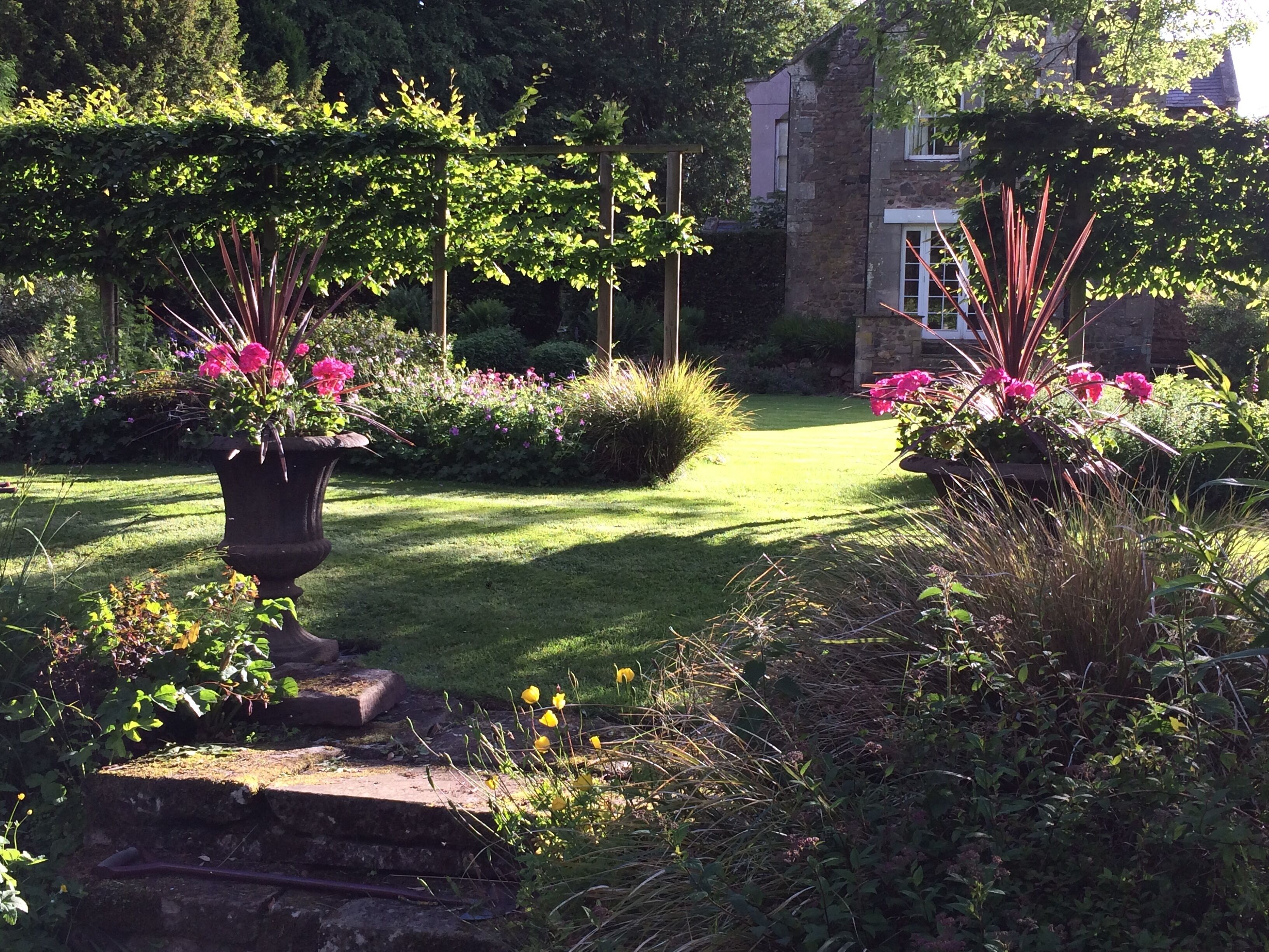 A garden with a paved pathway, flowering plants, and a stone wall.