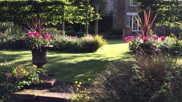 A garden with a paved pathway, flowering plants, and a stone wall.