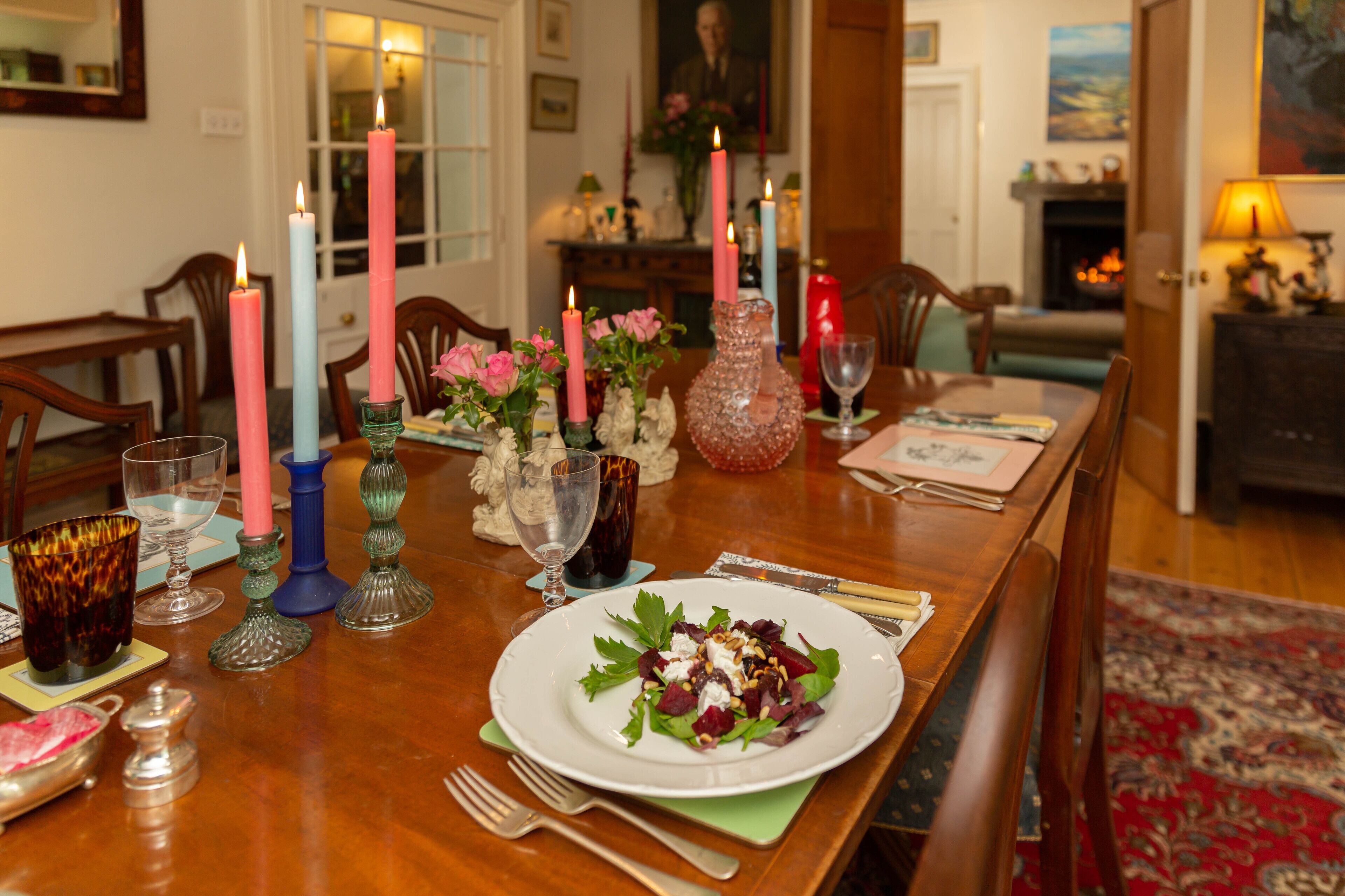 Una mesa de comedor con velas, un florero y un plato de ensalada.