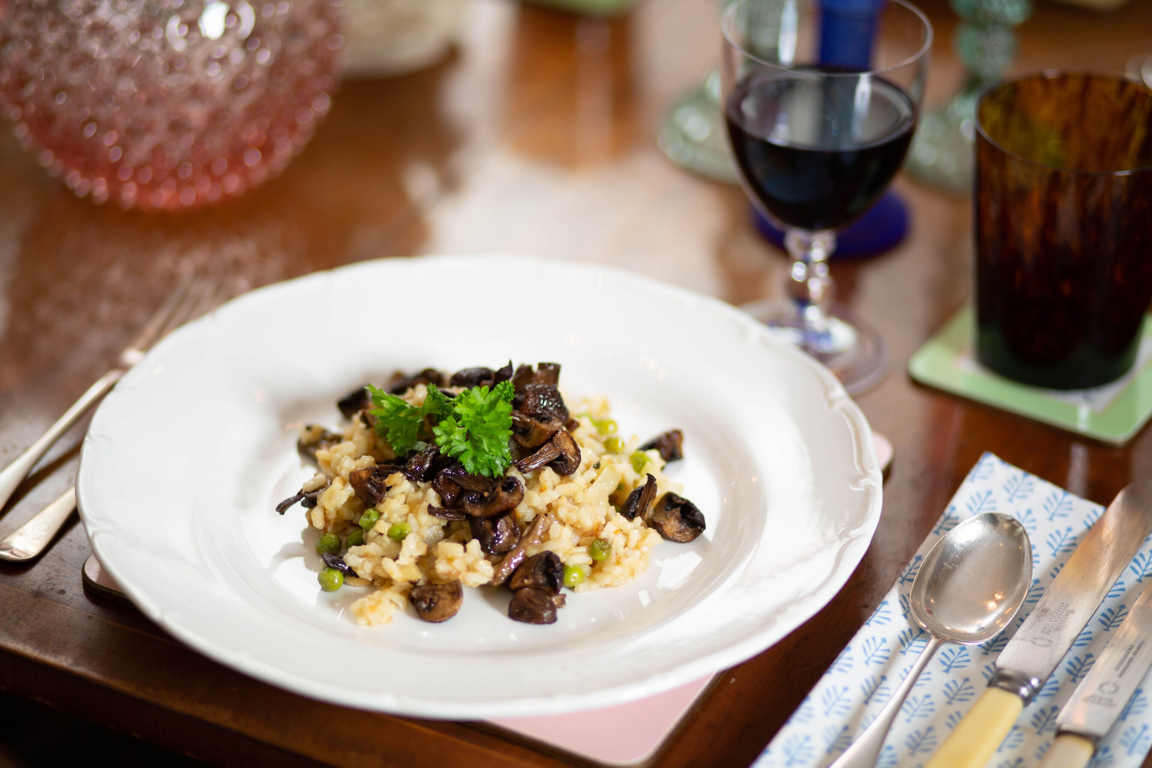 A plate of rice with mushrooms and peas, a spoon, a knife, and a glass of red wine on a table.