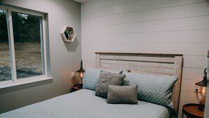 A bedroom with a bed, a window, a nightstand, and a wall-mounted shelf.