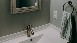 A bathroom with a white sink, a mirror with a distressed frame, a towel ring, and a wall-mounted light fixture.