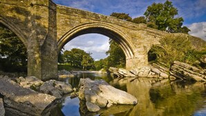 A stone bridge over a calm river with large rocks in the foreground. - Remarkable 1-bed Apartment in Kirkby Lonsdale (Carnforth)