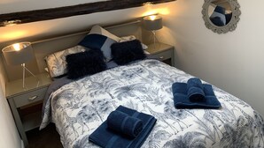 A bedroom with a skylight, a bed with patterned bedding, two bedside lamps, a mirror, and a folded towel on the bed. - Remarkable 1-bed Apartment in Kirkby Lonsdale (Carnforth)