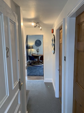 A hallway leading to a dining area with a clock and a lamp on the wall.