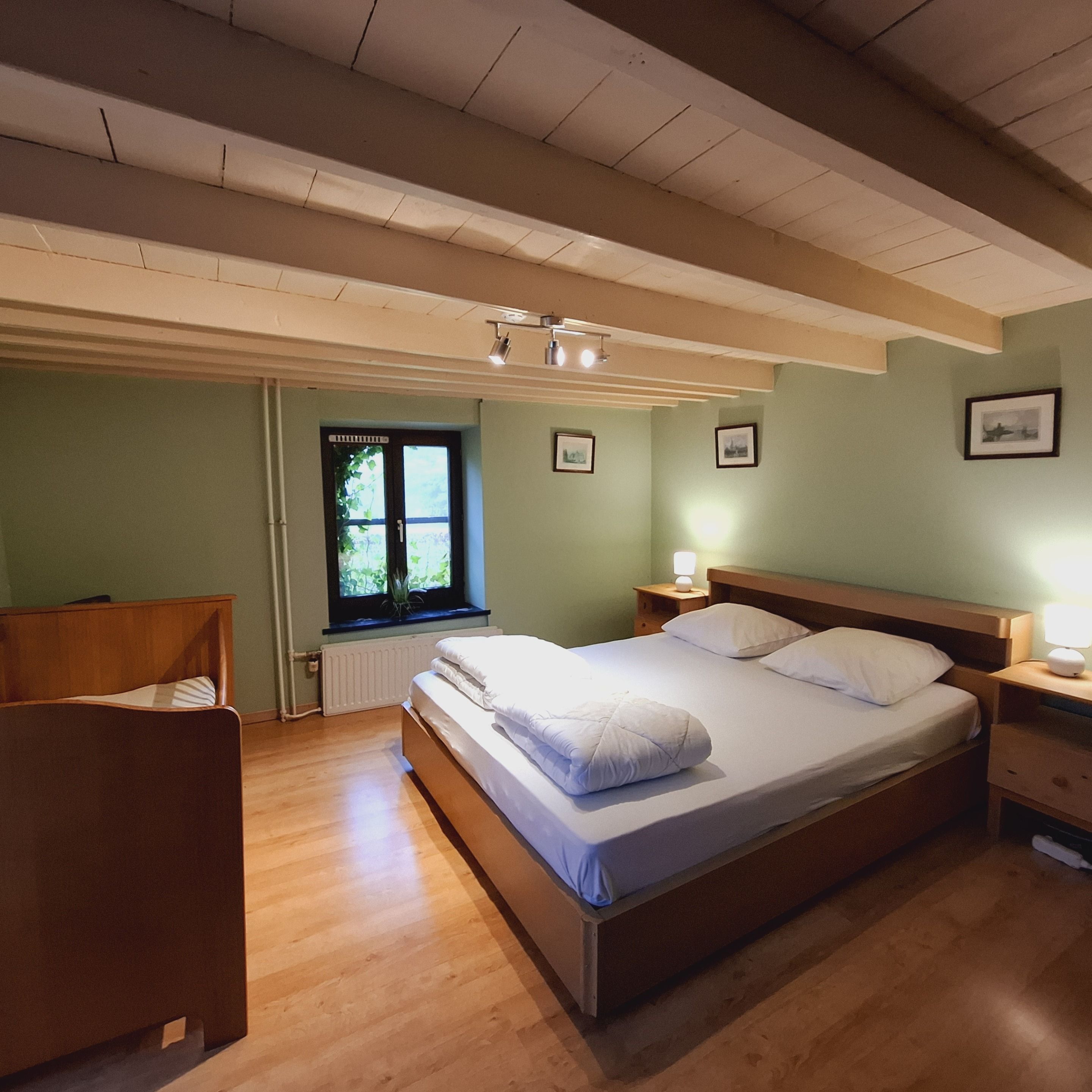 Een slaapkamer met een houten bed, nachtkastje, stoel, raam met uitzicht en een radiator.