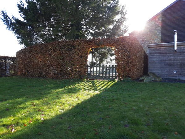 Un jardín con cerca de madera, un árbol grande y un edificio con muro de piedra.