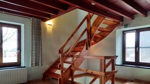 A wooden staircase structure in a room with wooden flooring, large windows, and a radiator.