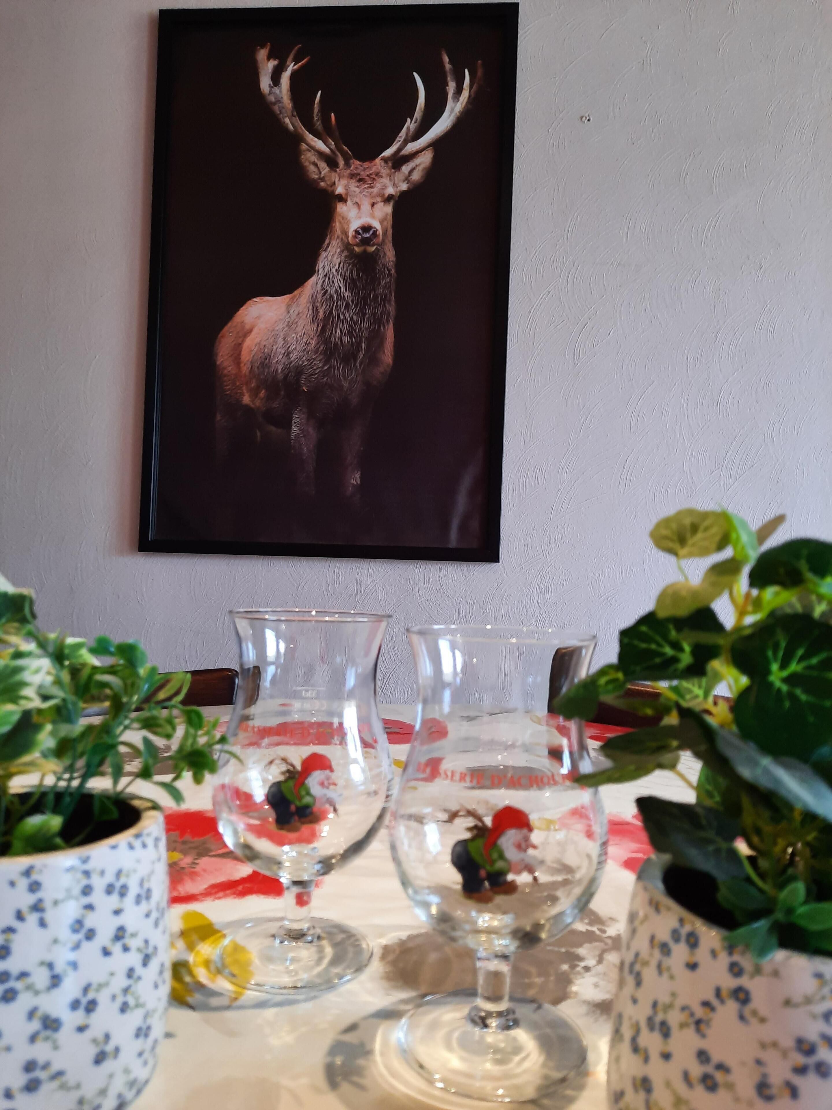 A dining table with clear glassware and a framed deer artwork above.