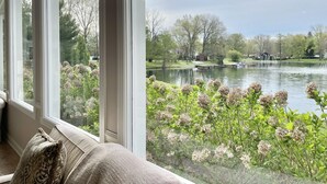 A view from a window overlooking a lake with a dock and a fountain, surrounded by trees and a well-maintained lawn. - Our Most Popular Lakefront Home (Carbondale)