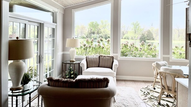 A cozy room with a large window, a lamp, a chair, and a table. - Our Most Popular Lakefront Home (Carbondale)