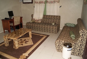 A living room with a patterned sofa, a wooden coffee table, a small table with a computer, and a white radiator.