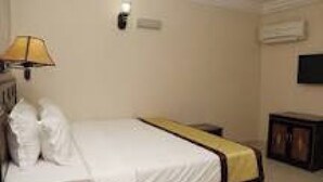 A hotel room with a bed, a lamp, a television, and a small cabinet. - Room-supreme Place Hotel - Guest Room (Abuja)