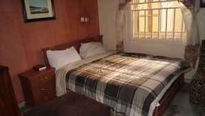 A bedroom with a bed, a nightstand, a wooden dresser, a bench, and a window with curtains. - Room-supreme Place Hotel - Guest Room (Abuja)