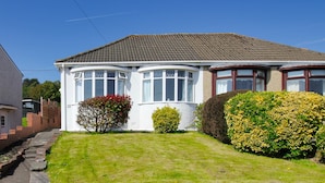 Une maison à deux étages, avec un toit en tuiles, de grandes fenêtres et une pelouse bien entretenue.