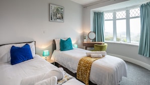 Une chambre d’hôtel avec deux lits, un bureau, une chaise, une fenêtre avec des rideaux et un tableau au mur.