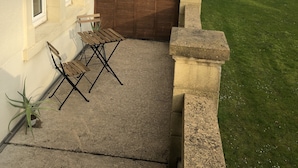 Un bâtiment à l’extérieur blanc, avec une clôture en bois et un petit patio comprenant une table et des chaises.