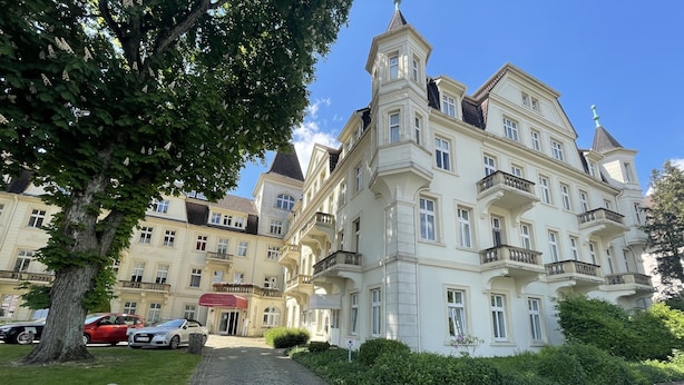 Un grand immeuble à plusieurs étages, doté d’une architecture classique, d’une allée pavée et de voitures garées.