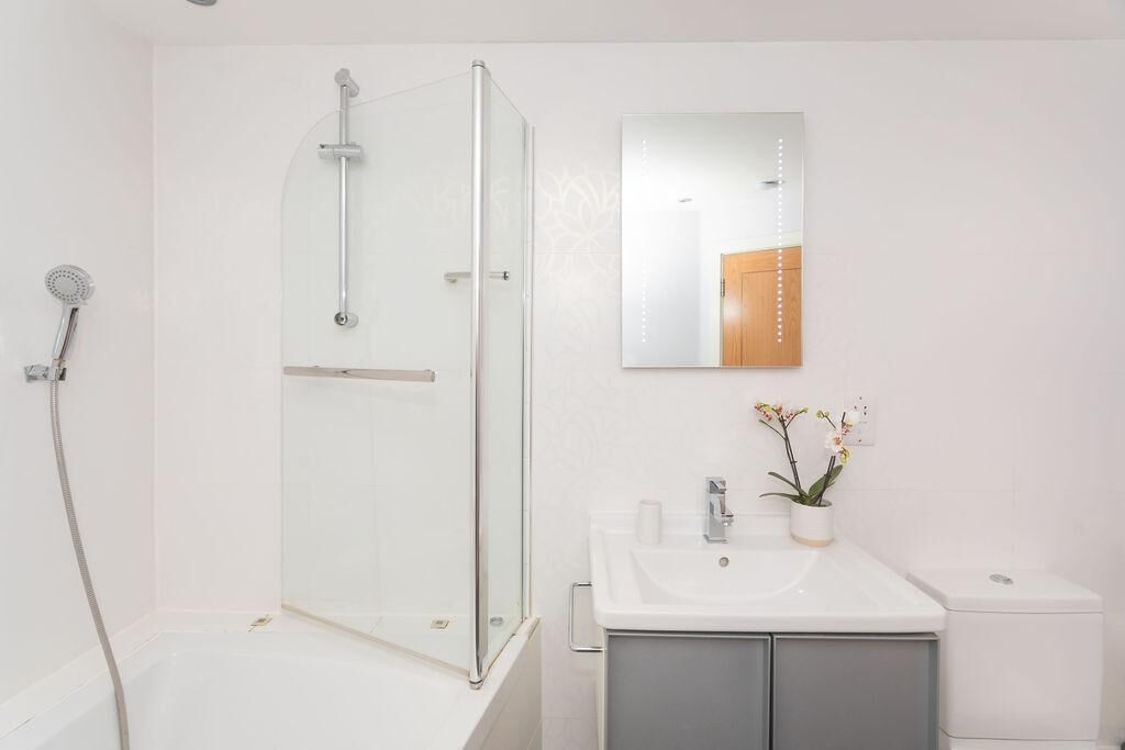A modern bathroom with a glass-enclosed shower, a white sink with a mirror above it, and a small potted orchid on the counter.
